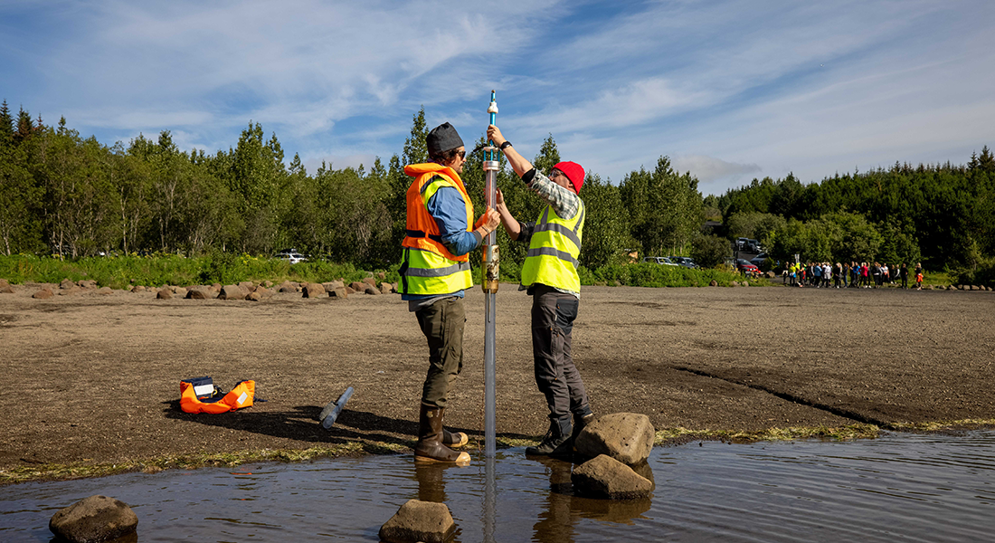 Two people drilling a hole in the ground to extract a sediment core.